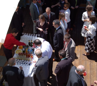 Grupo de personas en una recepci&oacute;n formal junto a una mesa con bebidas.