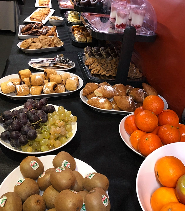 Buffet variado con frutas y reposter&iacute;a sobre una mesa con mantel negro.