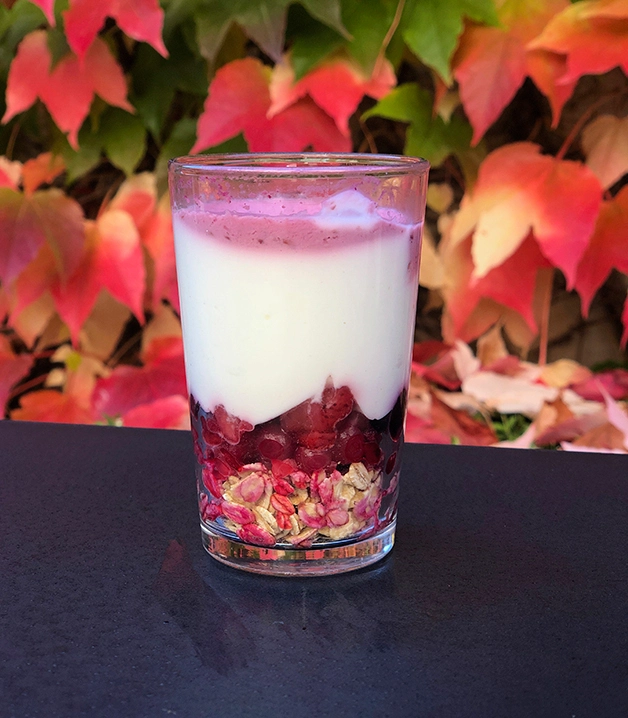 Vaso con yogur, frutos rojos y avena. Fondo de hojas oto&ntilde;ales.