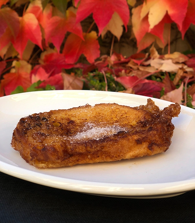 Torrija espolvoreada con az&uacute;car sobre un plato, fondo de hojas oto&ntilde;ales.