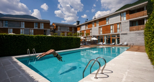 Persona zambull&eacute;ndose en una piscina en un complejo moderno con cielo despejado.