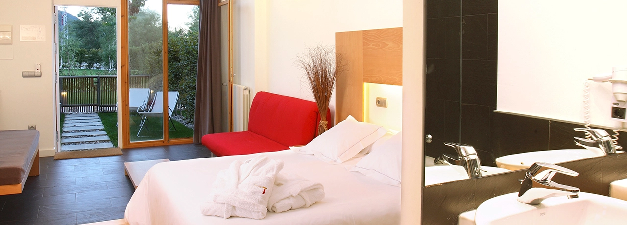 Habitación moderna con cama, sofá rojo y acceso a jardín exterior.