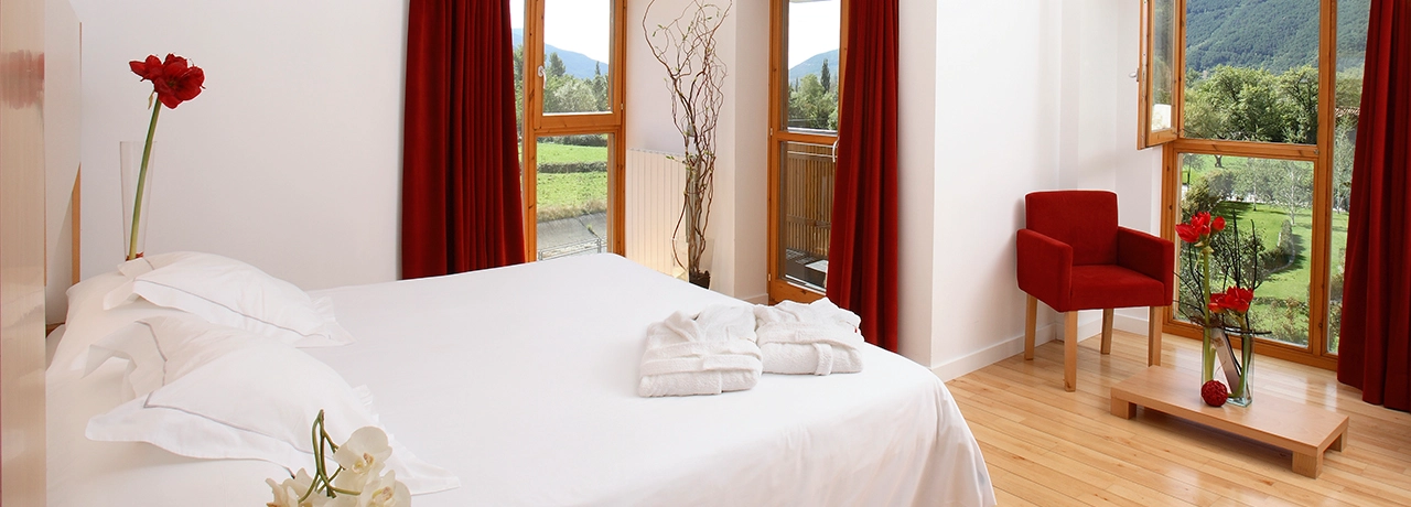 Habitación luminosa con cama blanca y cortinas rojas, vista al campo.