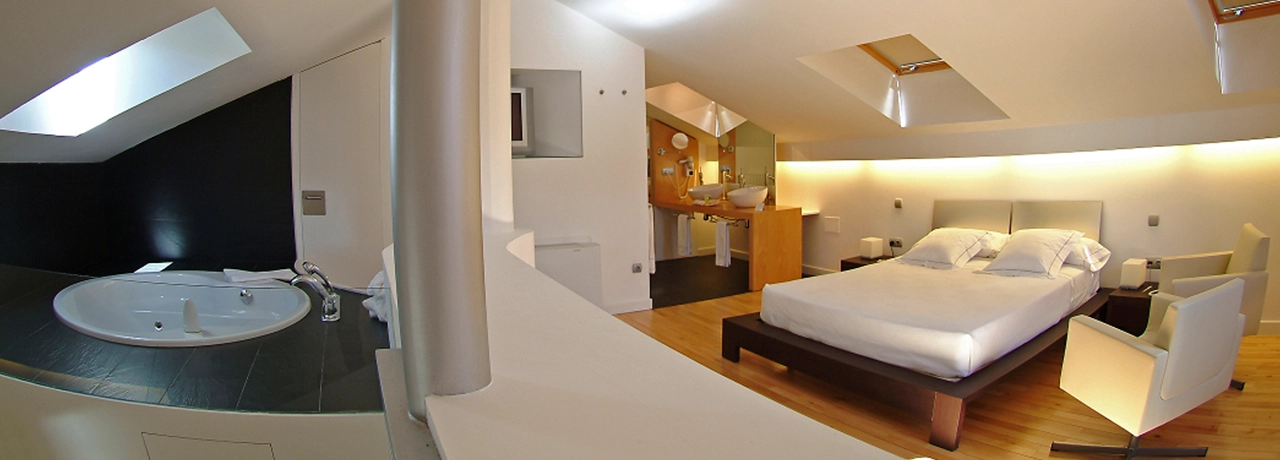 Habitación moderna con cama, jacuzzi, asiento y baño al fondo.