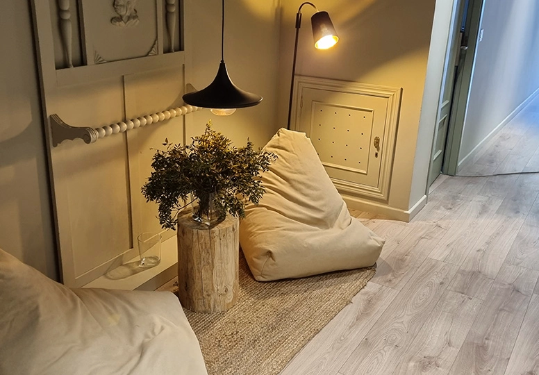 Espacio acogedor con l&aacute;mparas, cojines y planta sobre tronco de madera.