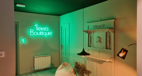 Habitaci&oacute;n con letrero ne&oacute;n verde "Tierra Boutique" y decoraci&oacute;n acogedora.
