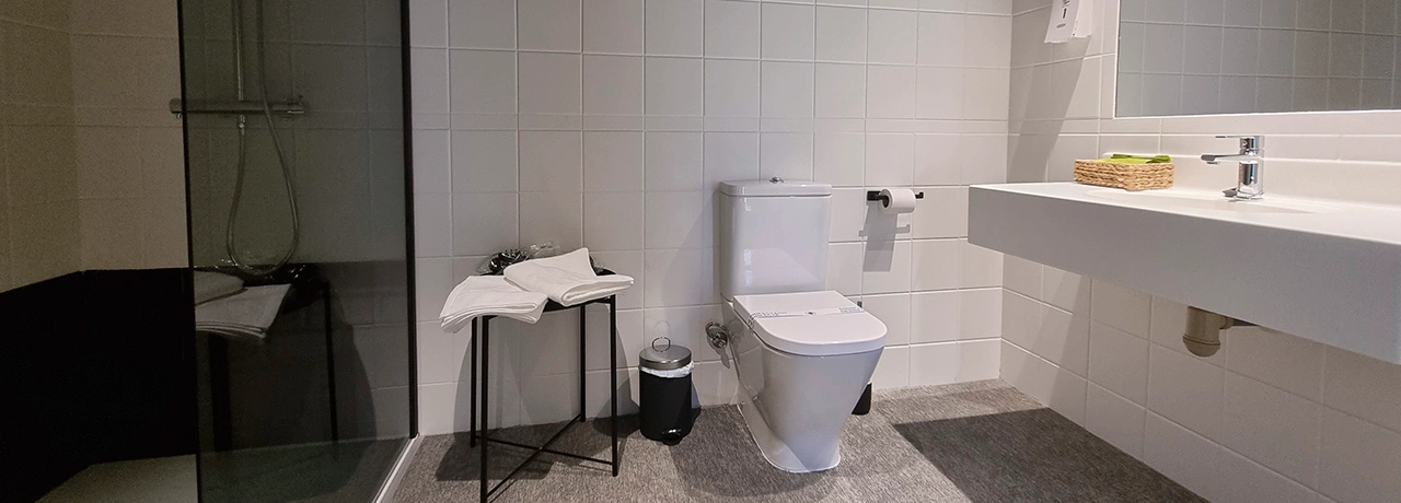 Ba&ntilde;o moderno con ducha, inodoro y lavabo minimalista en tonos claros.