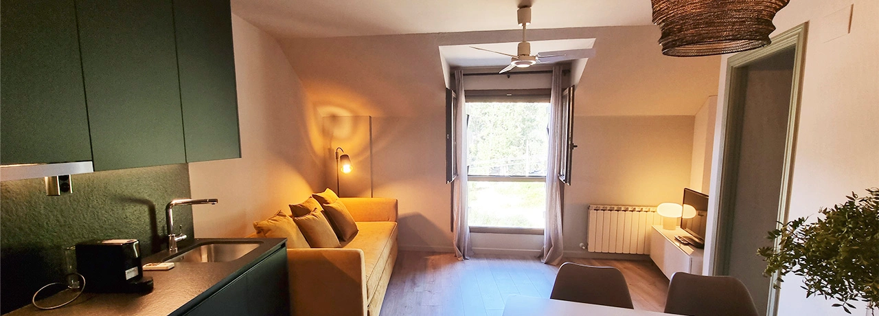 Sala moderna con cocina abierta, sof&aacute; amarillo y ventana grande iluminada.