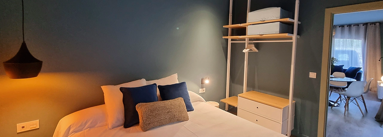 Habitaci&oacute;n moderna con cama, estante y vista a sala de estar.