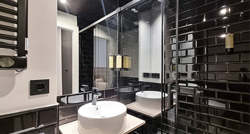 Ba&ntilde;o moderno con azulejos negros y lavabo blanco junto a una ducha de vidrio.