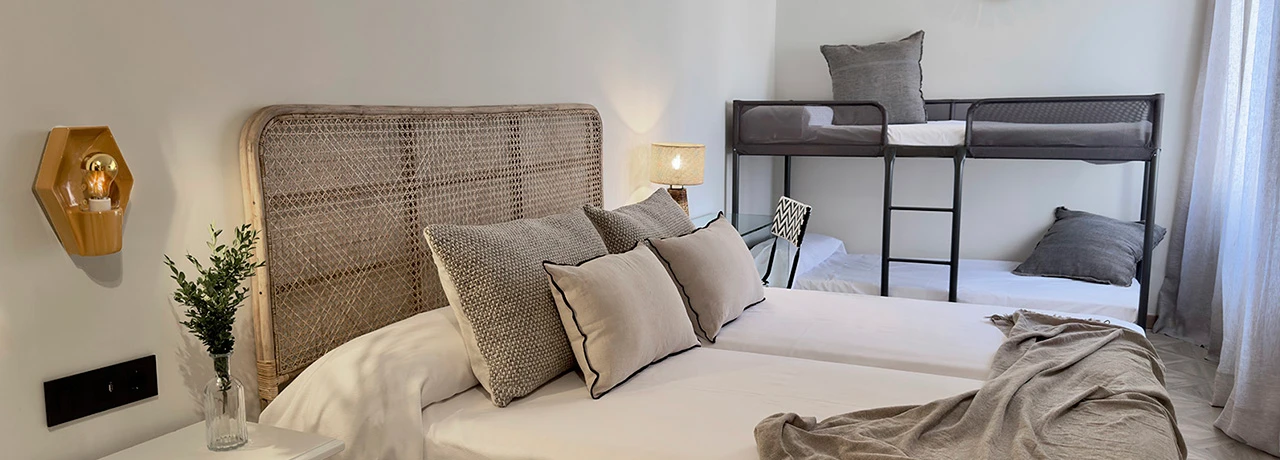 Habitación con cama, literas, cojines y lámpara de pared encendida.