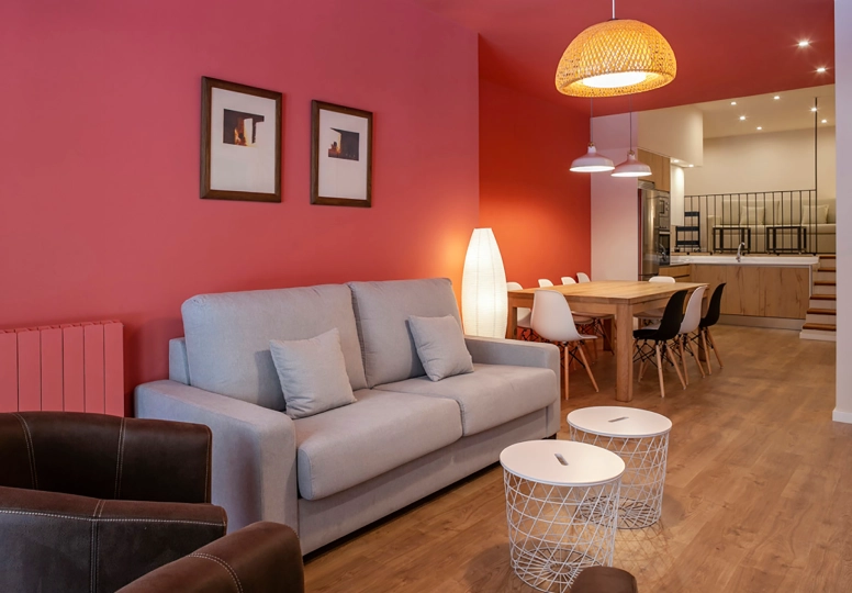 Sala moderna con sof&aacute; gris, pared roja y comedor al fondo.