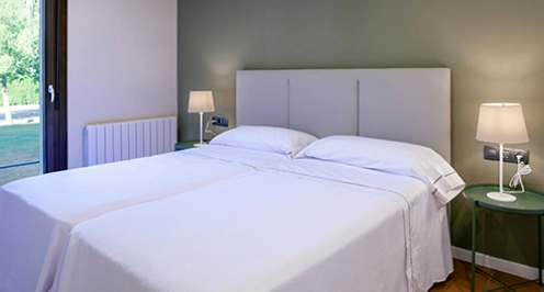 Habitaci&oacute;n con dos camas individuales, l&aacute;mparas de noche y ventana.