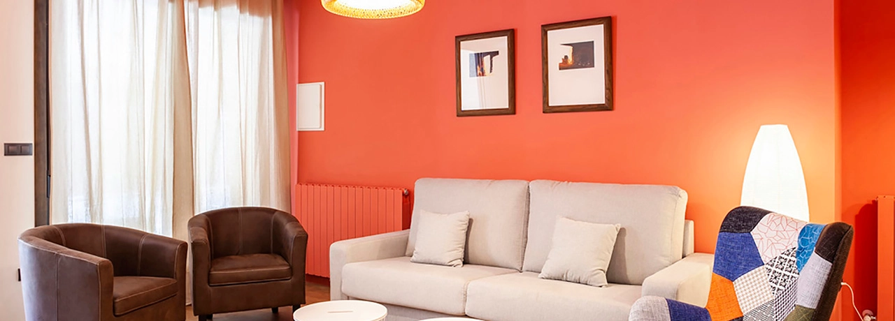 Sala moderna con pared roja, sof&aacute; gris, sillones marrones y l&aacute;mpara de pie.