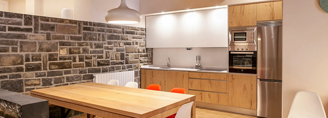 Cocina moderna con pared de ladrillo, mesa de madera y electrodom&eacute;sticos.