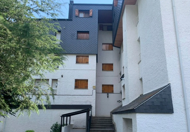 Edificio blanco de tres pisos con ventanas de madera y escalera exterior.