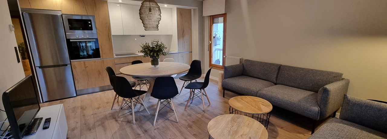 Sala y cocina moderna con muebles en tonos grises y madera clara.