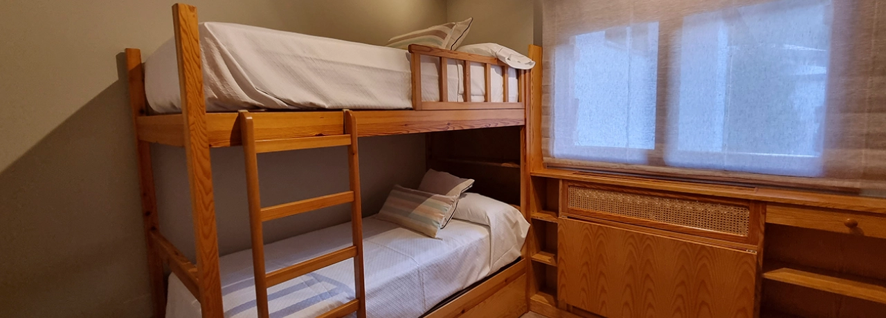 Litera de madera en habitación sencilla con ventana al fondo.