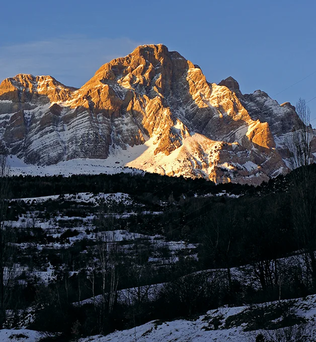 Montaña nevada iluminada por el sol en un paisaje al atardecer.