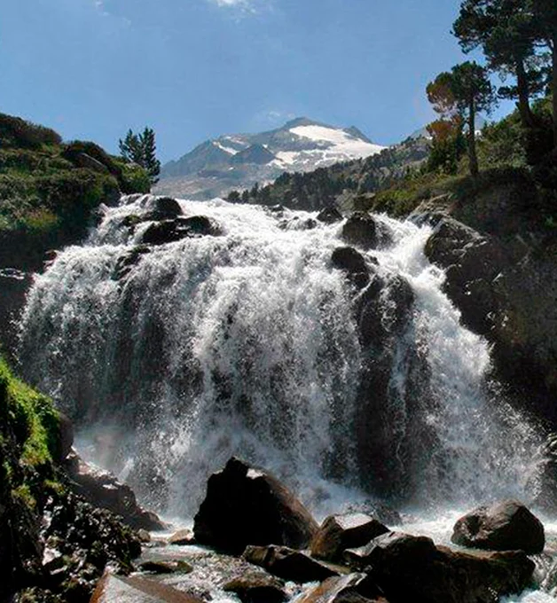 Cascada con montaña nevada de fondo bajo un cielo azul claro.