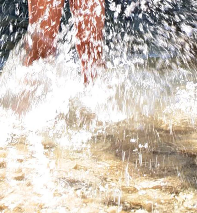 Piernas salpicando agua mientras camina en la orilla del mar.