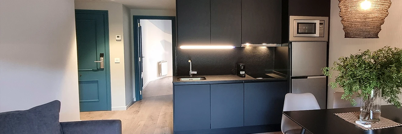 Cocina moderna con muebles negros, mesa y planta decorativa.