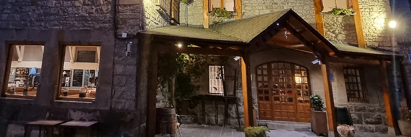 Fachada de una casa r&uacute;stica de piedra con ventanas y un tejado de madera.