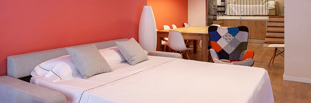 Dormitorio moderno con sof&aacute; cama, mesa de comedor y sill&oacute;n colorido.