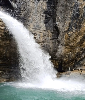 Cascada fluyendo sobre rocas hacia un charco turquesa.