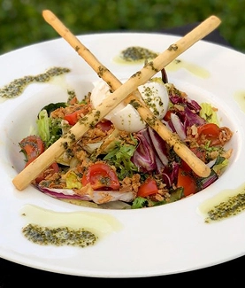 Ensalada con palitos de pan y aderezo verde en un plato blanco.