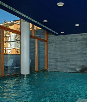 Piscina interior con techo azul y ventanas de madera al fondo.