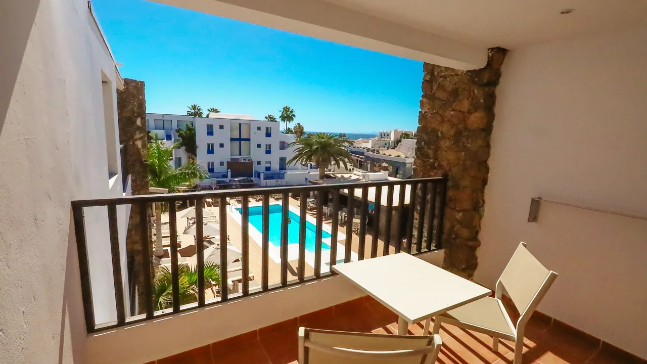 Vista desde balcón con piscina y edificios al fondo, cielo despejado.