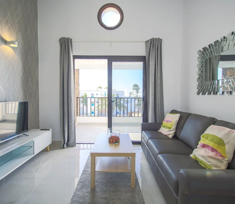 Sala moderna con sofá gris, mesa de centro y balcón con vista exterior.