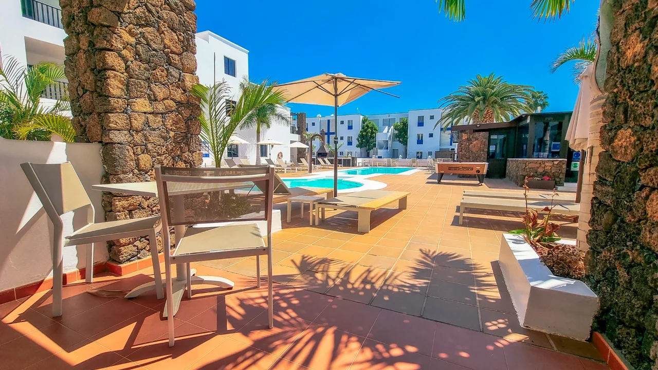Piscina al aire libre con sillas y palmeras bajo un cielo azul.