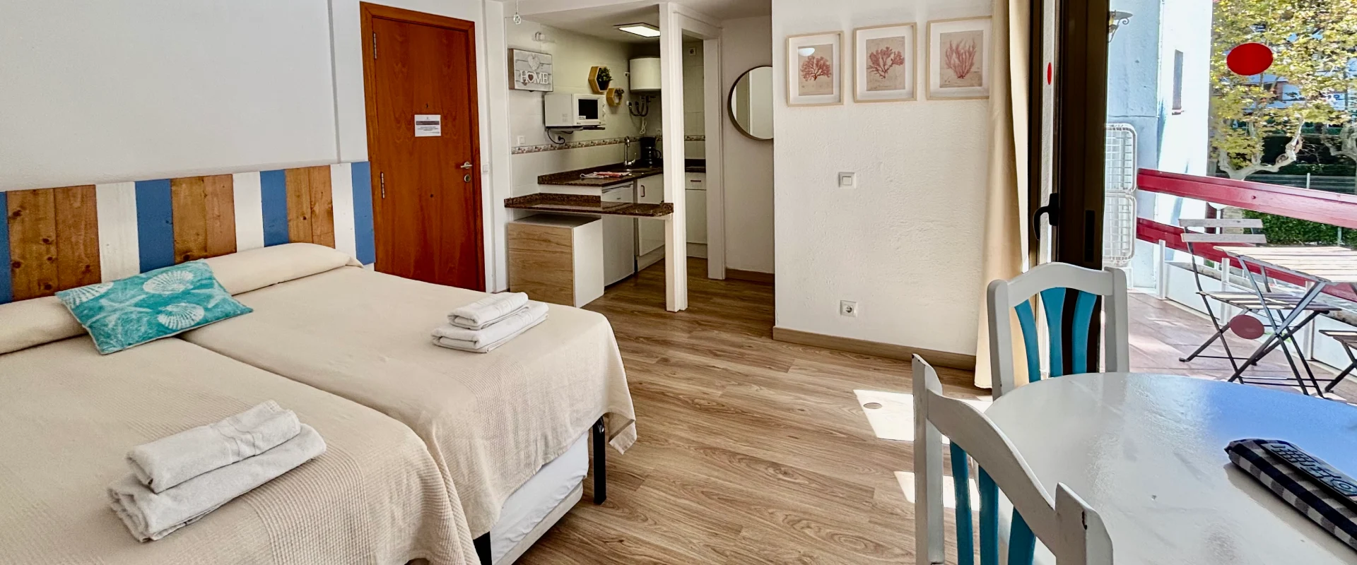 Habitaci&oacute;n con cama doble, cocina, mesa y balc&oacute;n iluminado.