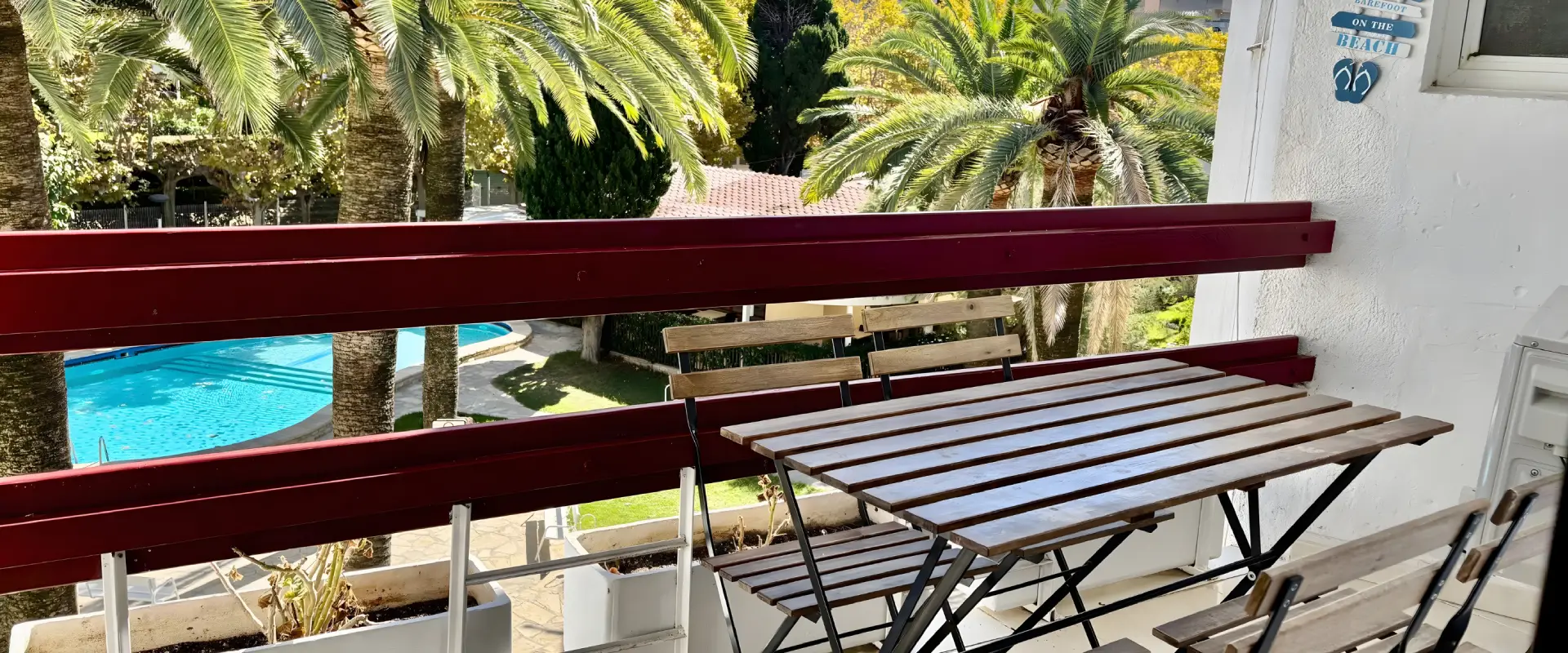 Balc&oacute;n con mesa, piscina y palmeras en el fondo.
