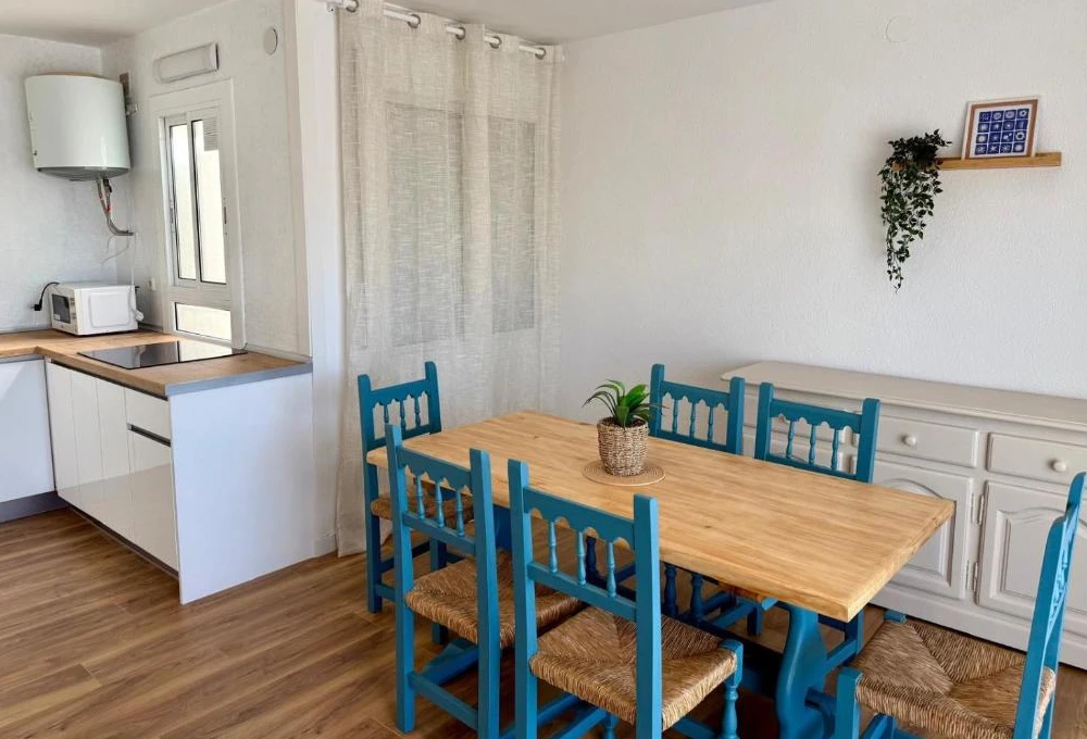 Cocina comedor con mesa de madera y sillas azules, decoraci&oacute;n sencilla.