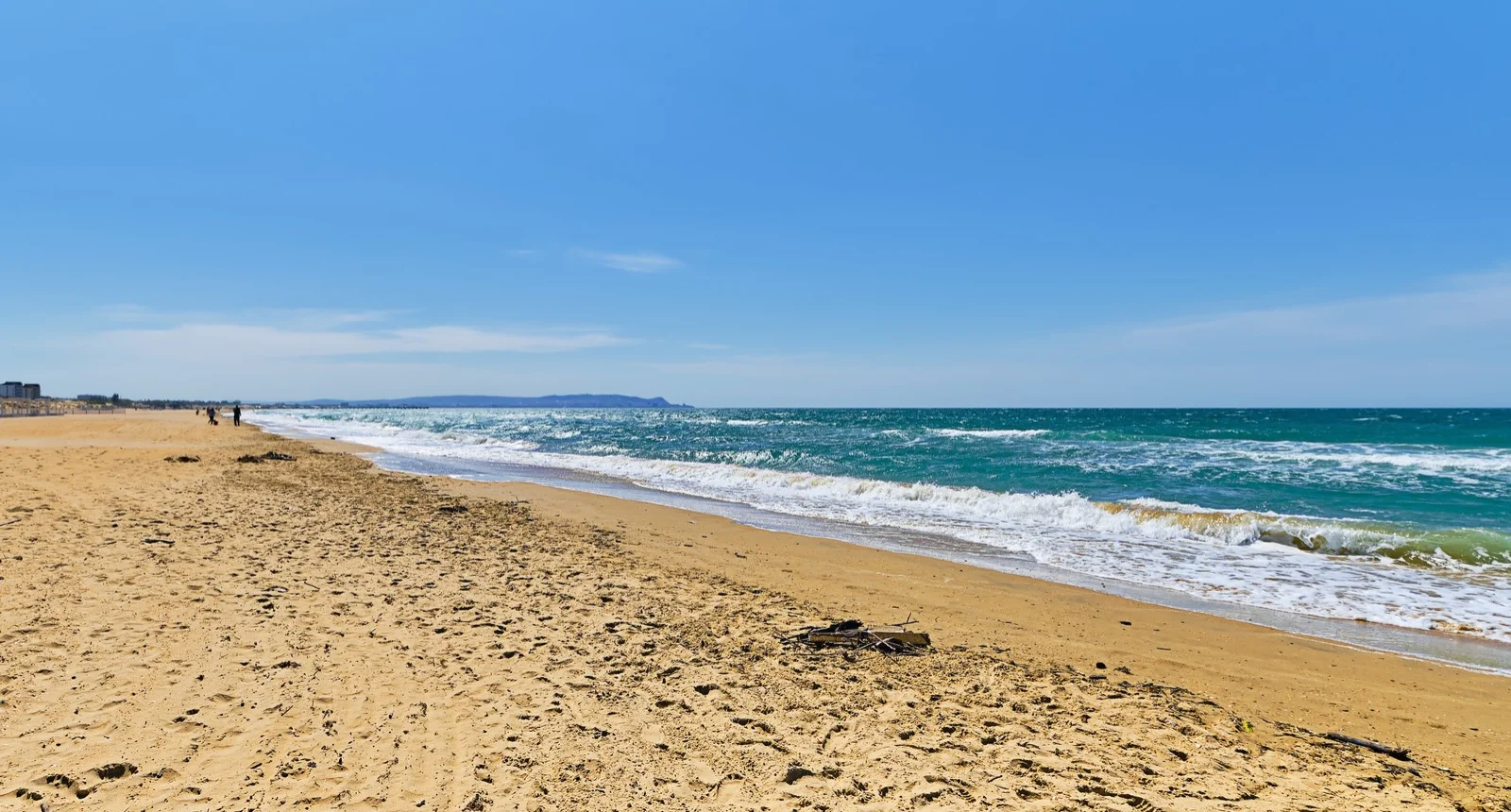 Playa soleada con arena y mar azul bajo un cielo despejado.