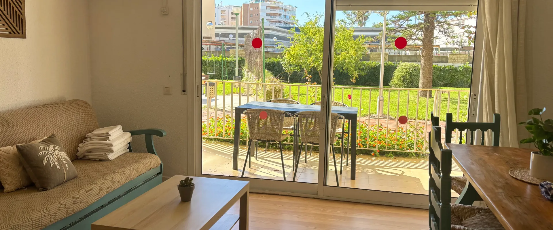 Sala luminosa con sof&aacute;, mesa y vista al jard&iacute;n a trav&eacute;s de ventanales.