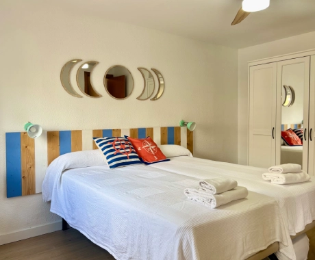 Habitaci&oacute;n con dos camas, espejos en la pared y ropa de cama blanca.