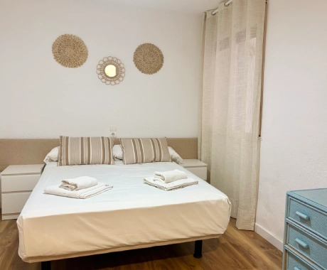 Dormitorio con cama doble, cojines, y decoraci&oacute;n en pared blanca.