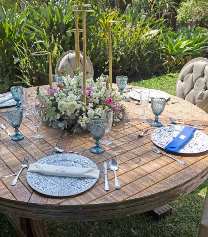 Mesa redonda decorada con flores y vajilla elegante en un jard&iacute;n.