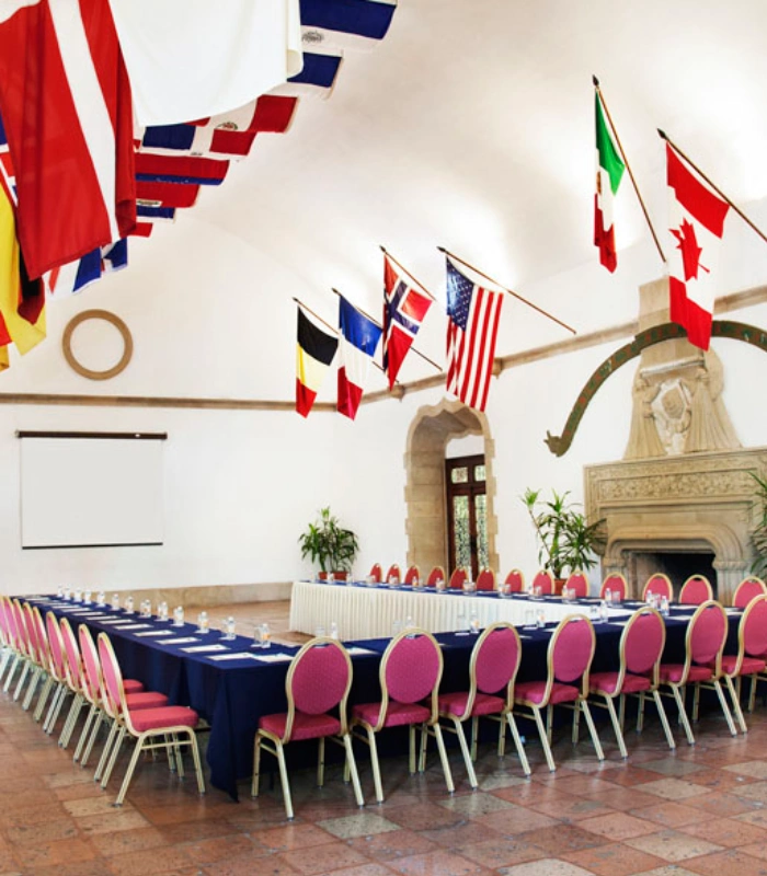 Sala de conferencias con banderas y sillas dispuestas en U.