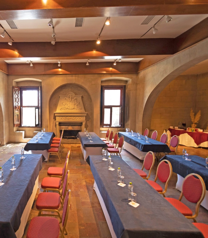 Sala de conferencias elegante con mesas largas, sillas rojas y chimenea decorativa.