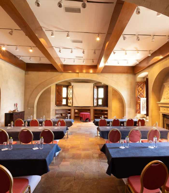 Sala de conferencias con mesas, sillas y pantalla de proyecci&oacute;n al fondo.