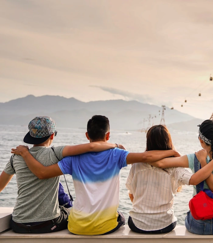Cuatro personas sentadas de espaldas miran el mar al atardecer.