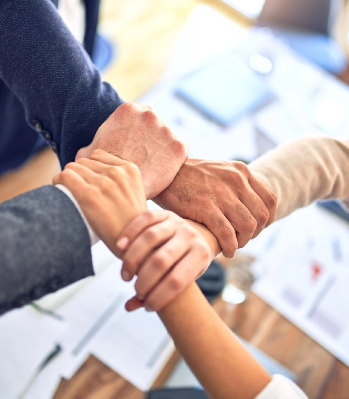 Cuatro manos unidas en un gesto de colaboraci&oacute;n sobre una mesa.