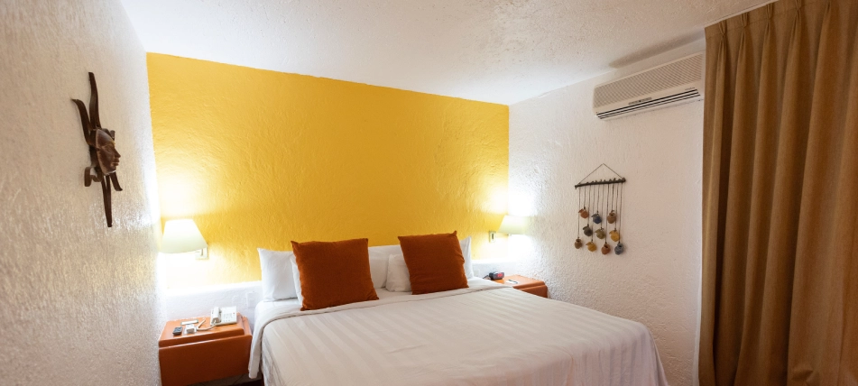 Habitaci&oacute;n con cama doble, pared amarilla, l&aacute;mparas y cortinas marrones.