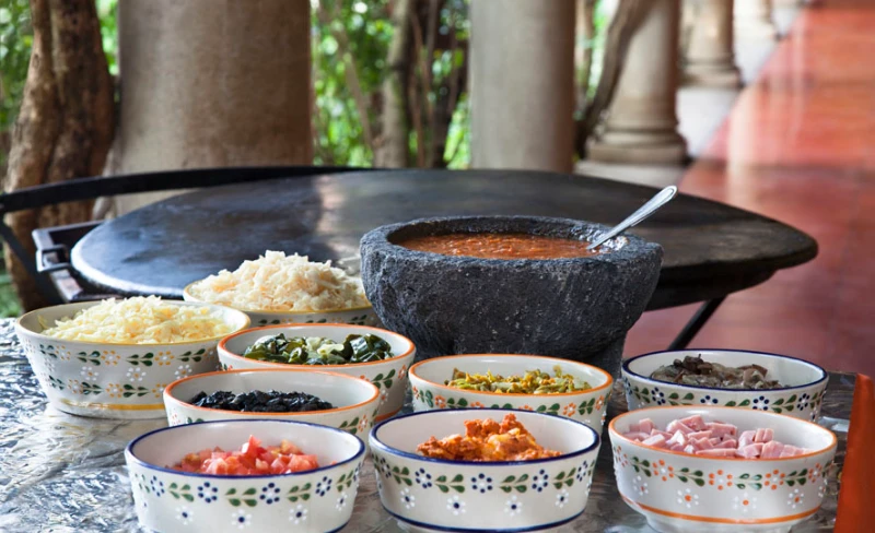 Mesa con cuencos de comida y un mortero de piedra en jard&iacute;n tropical