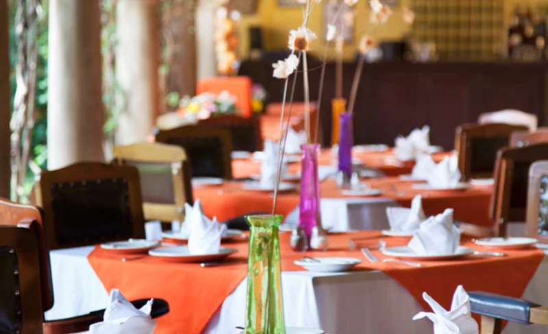Mesa de banquete con manteles naranjas y jarras, decorada para evento.